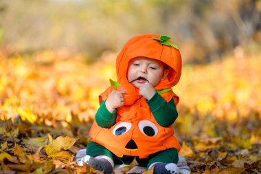 Sonbahar yapraklarının arka planında balkabağı kostümlü neşeli çocuk.