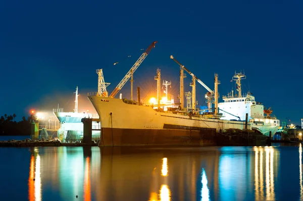 Cargo ship  under repair by sand blasting in floating dry dock at night