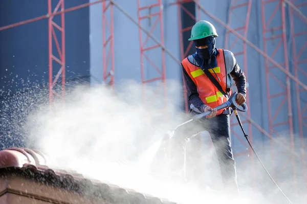 Worker in safety vest cleaning roof tiles with high pressure cleaning machine. Roof cleaning with high pressure water jet