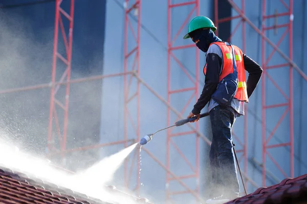 Worker in safety vest cleaning roof tiles with high pressure cleaning machine. Roof cleaning with high pressure water jet