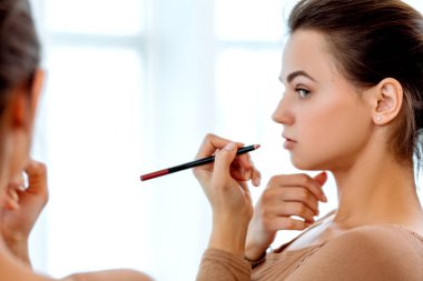 Kadın bir ayna önünde kırmızı ruj dudakları boyalar