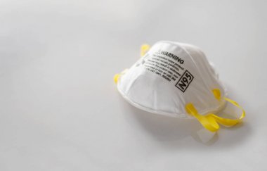 N95 hava filtresi maskesi. Beyaz masadaki kişisel koruyucu ekipman yumuşak odaklı ve arka plandaki ışığın üzerinde