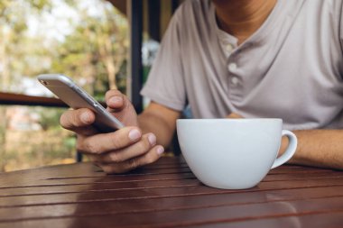 Kafede oturan bir adamın elindeki akıllı telefonların yakın plan görüntüsü ve arka planda ışık var.
