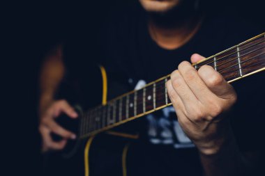 Karanlık odada gitar çalan yakın plan bir adam yumuşak odaklı ve arka planda ışık üzerinde 01