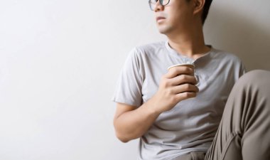 Yakın plan, odada kağıt kahve bardağını tutarken arka planda hafif bir odaklanma ve ışık var.