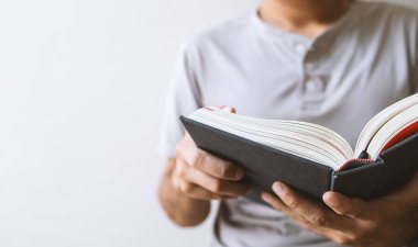 Genç adam pencerenin önünde oturmuş, arka planda hafif bir odaklanma ve ışıkla kitap okuyor.