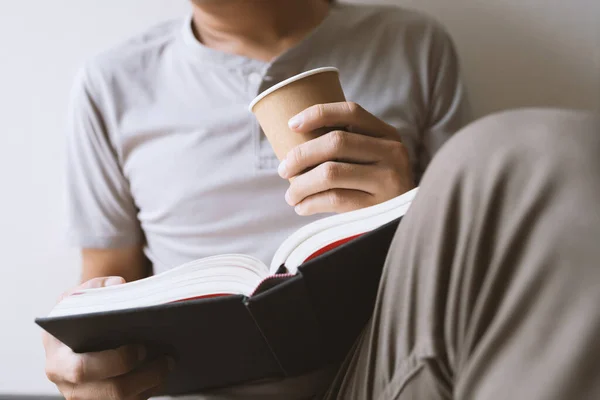 Ung Man Sitter Och Läser Bok Medan Håller Papperskopp Kaffe — Stockfoto