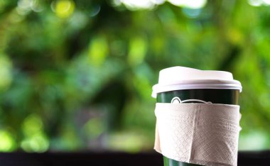 Kağıt bardaktaki sıcak kahveyi ahşap masaya koy. Yumuşak odaklı ve arka planda ışık olsun.