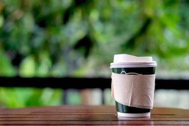 Kağıt bardaktaki sıcak kahveyi ahşap masaya koy. Yumuşak odaklı ve arka planda ışık olsun.