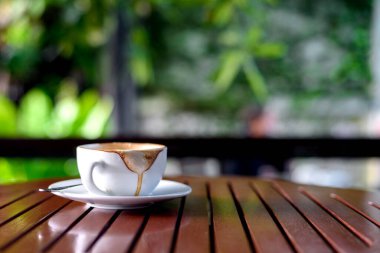 hot coffee that has almost been drunk on wood table with soft-focus and over light in the background