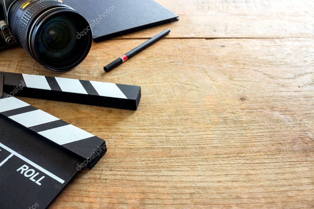 film director's desk. clapboard, book and digital camera on wood table with soft-focus and over light in the background 