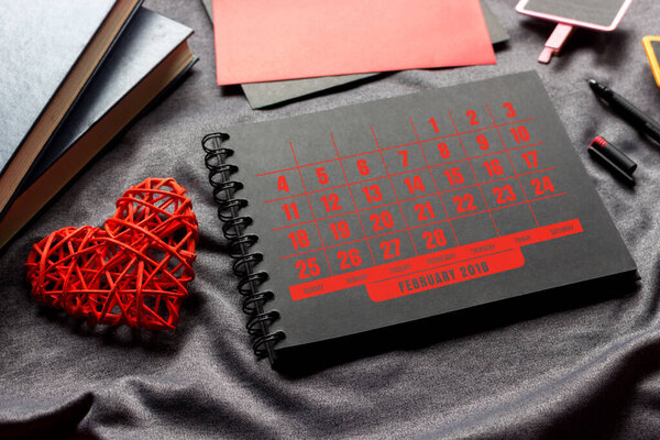 valentine's day concept.  black book, red heart and pen on gray cloth with over light in the background. space for text