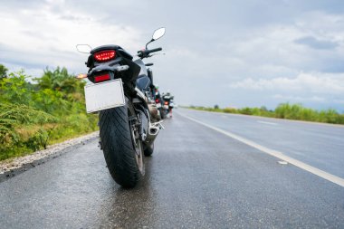 Yakın plan motosiklet motosikleti, yağmurlu bir yolda, ıslak bir yolda, arka planda hafif bir odaklanma ve ışık altında bir su birikintisinin içinden geçiyor.