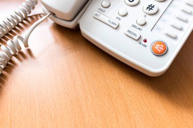 Masanın üzerindeki beyaz telefonu kapat. Arka planda hafif odaklı ve ışığın üzerinde.