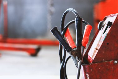 Araba tamirhanesinde akü şarj cihazını kapat. Arka planda hafif odaklı ve ışığın üstünde.