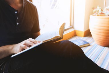 Genç adam arka planda yumuşak bir odak ile pencerenin önünde oturmuş kitap okuyor. ışık ve vintage renk tonunun üzerinde