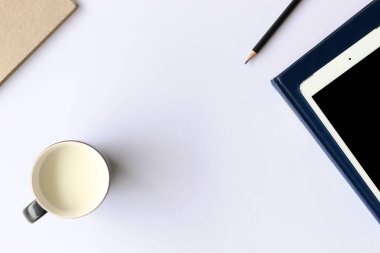 Bir fincan süt, tablet bilgisayar ve arka planda yumuşak odaklı beyaz ahşap masa üzerine kitap. ışığın üzerinde. stilsel kırsal.