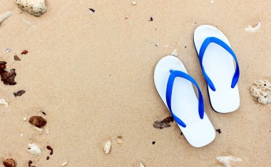 Kumlu bir okyanus sahilinde, ışığın üstünde terlikler.