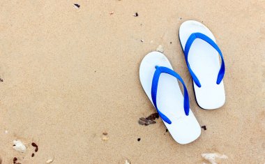 Kumlu bir okyanus sahilinde, ışığın üstünde terlikler.