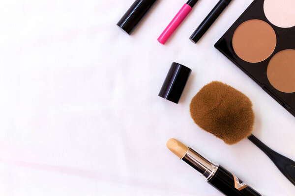 makeup cosmetics and brushes on white fabric background, over light