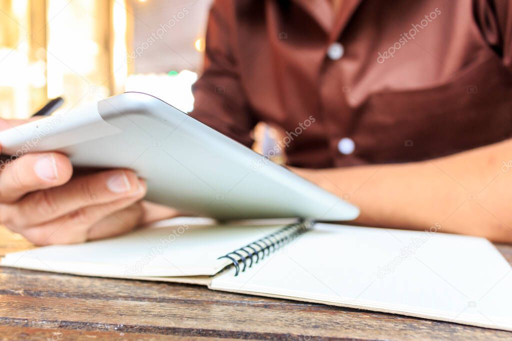 businessman writing notes from ipad mini at coffee shop. selective focus, over light