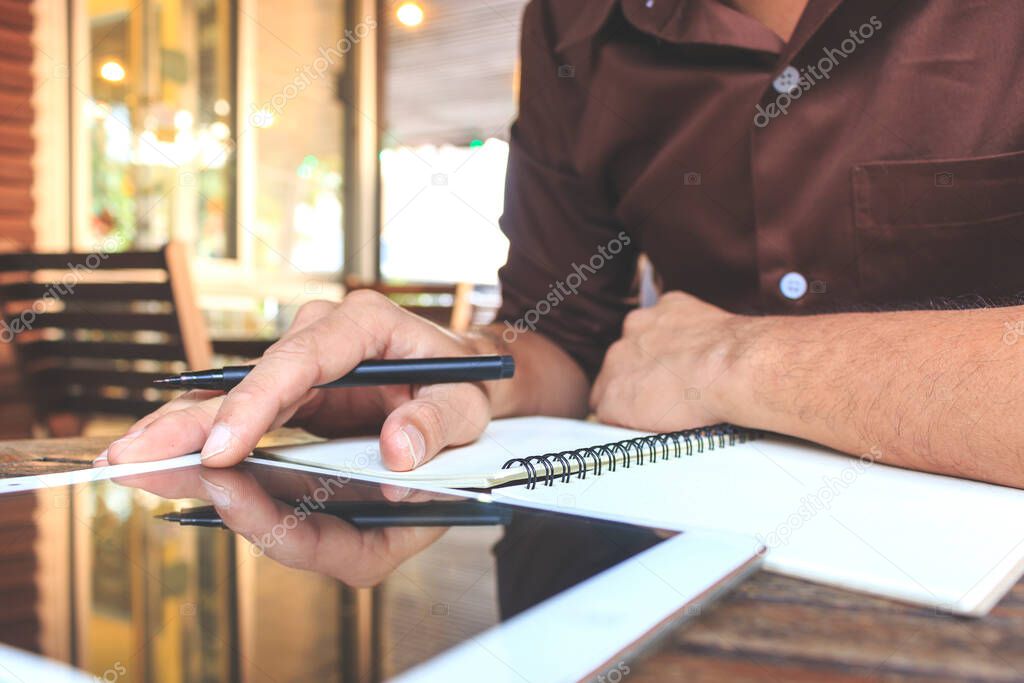 businessman writing notes from ipad mini at coffee shop. selective focus, over light and film color tone