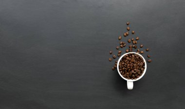 Siyah ahşap zemin üzerinde beyaz fincanda kahve çekirdeği. Üst Manzara. Metin için boşluk