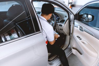 Otomobil tamircisi, arka planda hafif odaklı ve ışıktan oluşan bir arabayı kontrol ediyor.