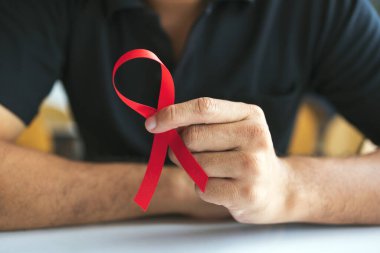 AIDS 'le savaşmak için kırmızı kurdeleli genç bir adam. Yumuşak odaklı ve arka planda ışık var.