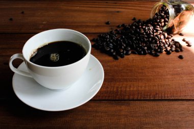 Bir fincan kahve ve bir kahve çekirdekleri eski ahşap tahta üzerinde cam kavanozda.