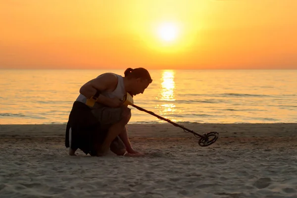 Człowiek za pomocą wykrywacza metali na plaży w zachód słońca — Zdjęcie stockowe
