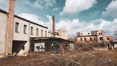 Terk edilmiş eski fabrika binası mavi bulutlu gökyüzü altında.