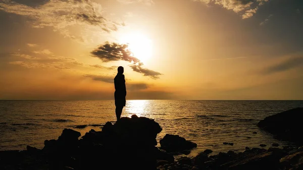 Силует чоловіка, що стоїть на скелі на пляжі під час заходу сонця — стокове фото