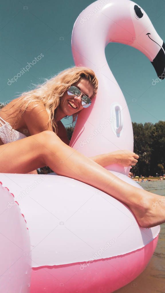 Summer lifestyle portrait of smiling girl having fun on pink flamingo inflatable mattress on the lake Balaton, Hungary. Wearing bikini and mirrored sunglasses. Positive emotions, portrait capture. 
