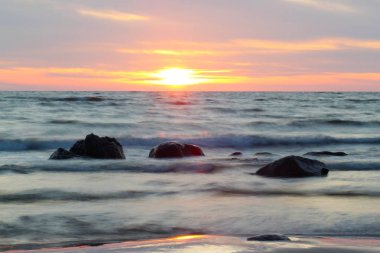 Gün batımında veya gün doğumunda güzel kayalık deniz kıyısı. Uzun pozlama manzara. Letonya yakınlarındaki Baltık denizi.