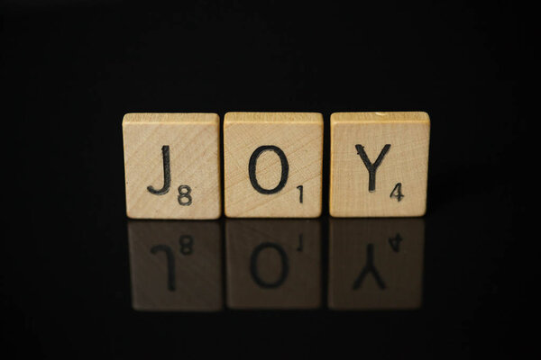 WOODBRIDGE, NEW JERSEY - November 9, 2018: Scrabble tiles spell out the word joy on a reflective black background