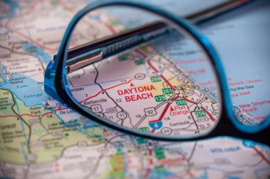 WOODBRIDGE, NEW JERSEY - July 13, 2020: A map of Florida is shown with a focus on Daytona Beach through a pair of eyeglasses. clipart