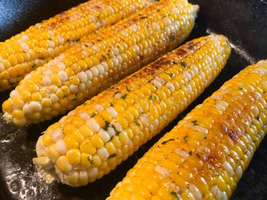 Taze Jersey Mısır koçanı sobadaki siyah dökme demir tavada pişirilir. Tereyağı, biber ve maydanozla kaplı..