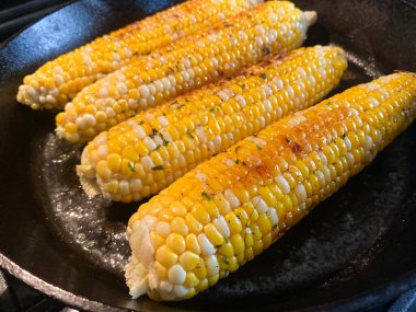 Taze Jersey Mısır koçanı sobadaki siyah dökme demir tavada pişirilir. Tereyağı, biber ve maydanozla kaplı..