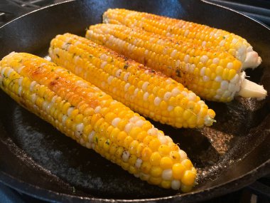 Taze Jersey Mısır koçanı sobadaki siyah dökme demir tavada pişirilir. Tereyağı, biber ve maydanozla kaplı..