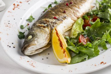 Limon ve beyaz plaka üzerinde taze sebze pişmiş balık 