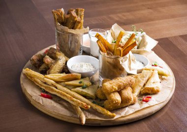 Farklı bira aperatifler: kalamar halkaları, patates kızartması, sıcak kanatları, ekmek ve ahşap tahta üzerinde soslar