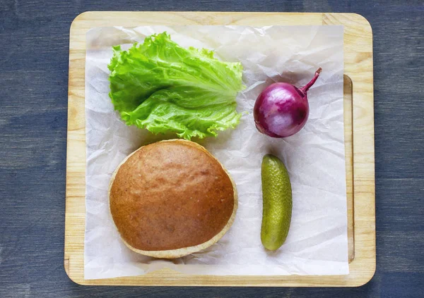 Burger topuz, soğan, marul ve ahşap tahta üzerinde turşu salatalık için malzemeler
