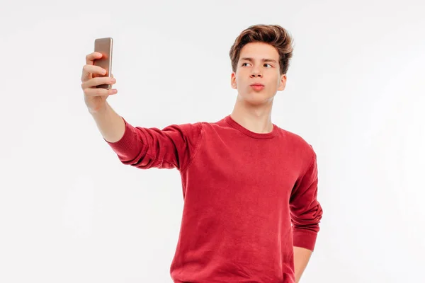 Jovem atraente faz uma selfie com smartphone no fundo branco — Fotografia de Stock