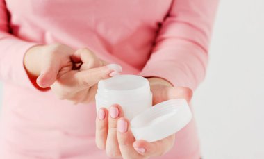 Hassas güzel kadınların elleri pembe manikür bakım krem gri arka plan üzerinde izole kavanoz holding ile yakın çekim