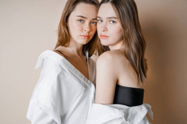 İki kız kardeş ikiz güzel çıplak kız kameraya bej renkli arka plan üzerinde arıyor izole moda modelleri