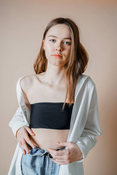 Модель красивая обнаженная девушка в белой рубашке, смотрящая в камеру на бежевом фоне
