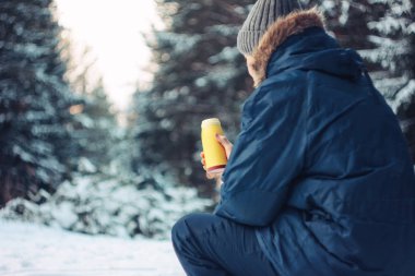Termos içinde elleri ile düşmüş ağaç üzerinde oturan kış ormandaki adam gezgin forester avcı