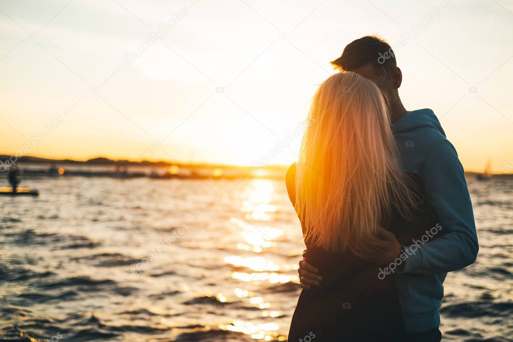Silhouette of couple in love on the pier, sunset time, water background