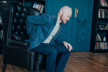 Çekici kel sakallı adam sırtı onun deri sandalye almaya çalışırken tutuyor. Zengin insanlar çok ağlar